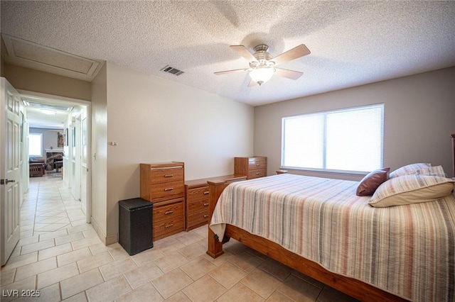 bedroom with a ceiling fan, visible vents, a textured ceiling, and light tile patterned floors