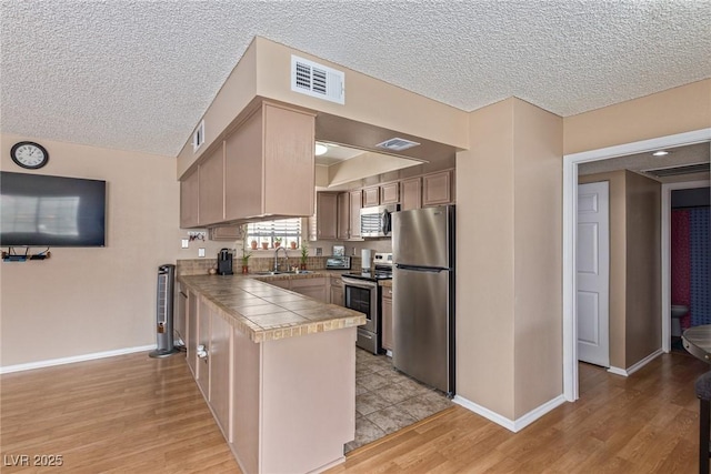 kitchen featuring visible vents, appliances with stainless steel finishes, a sink, light wood-type flooring, and a peninsula