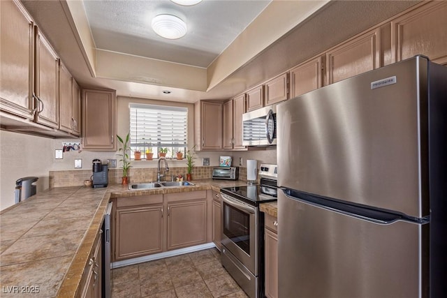 kitchen with light tile patterned floors, appliances with stainless steel finishes, a raised ceiling, and a sink