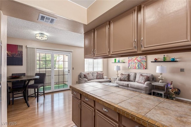 kitchen with visible vents, tile countertops, light wood-style flooring, open floor plan, and a textured ceiling