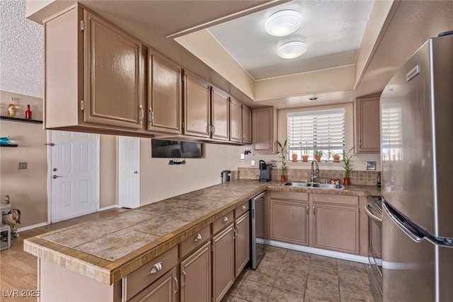 kitchen featuring a tray ceiling, appliances with stainless steel finishes, a sink, and tile counters