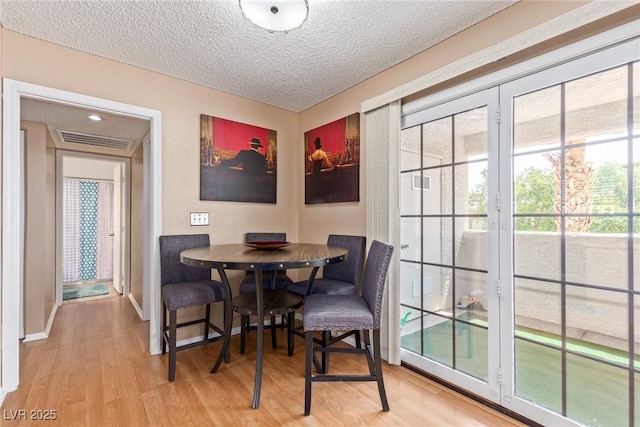 dining room with a textured ceiling, visible vents, wood finished floors, and french doors