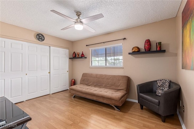 sitting room with ceiling fan, light wood finished floors, a textured ceiling, and baseboards