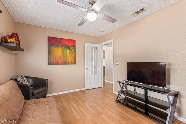 living room with a textured ceiling, a ceiling fan, baseboards, visible vents, and light wood-style floors