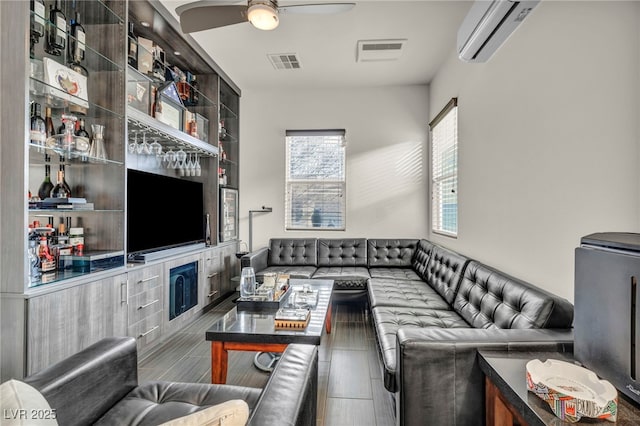 living area with visible vents, a ceiling fan, and a wall mounted air conditioner