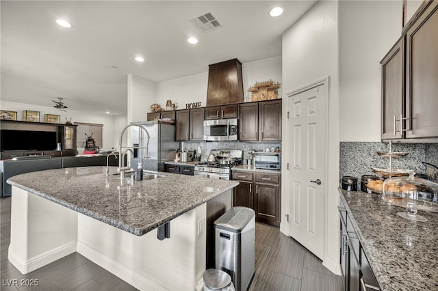 kitchen with stainless steel appliances, a breakfast bar area, a center island with sink, and dark brown cabinetry