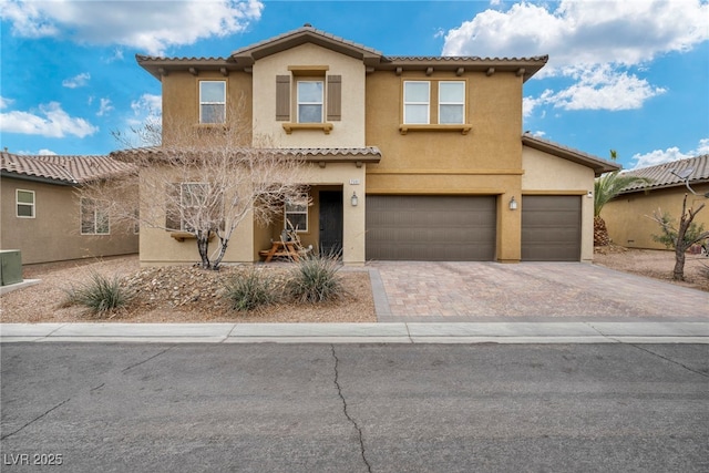 mediterranean / spanish home with a garage, a tiled roof, decorative driveway, and stucco siding