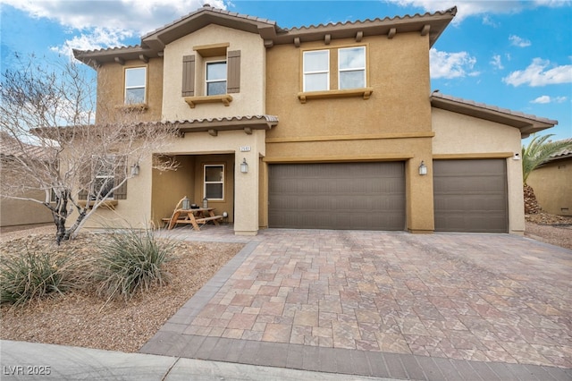 mediterranean / spanish-style house with an attached garage, a tiled roof, decorative driveway, and stucco siding