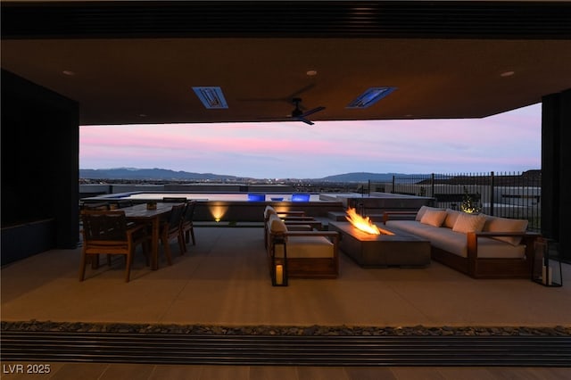 patio terrace at dusk featuring an outdoor fire pit, a mountain view, fence, and outdoor dining area