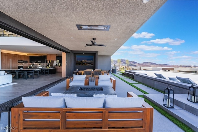 view of patio / terrace featuring a ceiling fan, outdoor dining area, an outdoor living space with a fire pit, and a mountain view