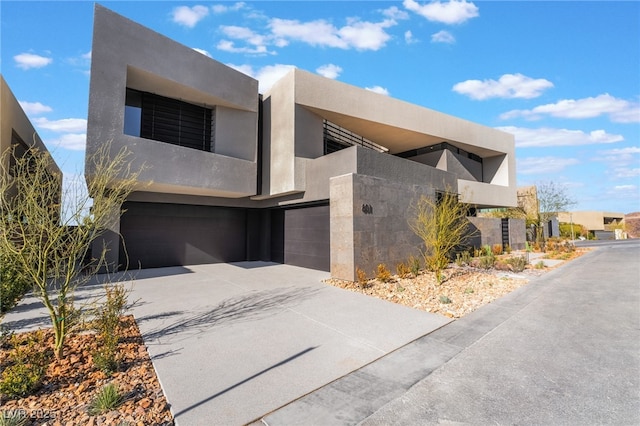 modern home featuring driveway, a balcony, an attached garage, and stucco siding