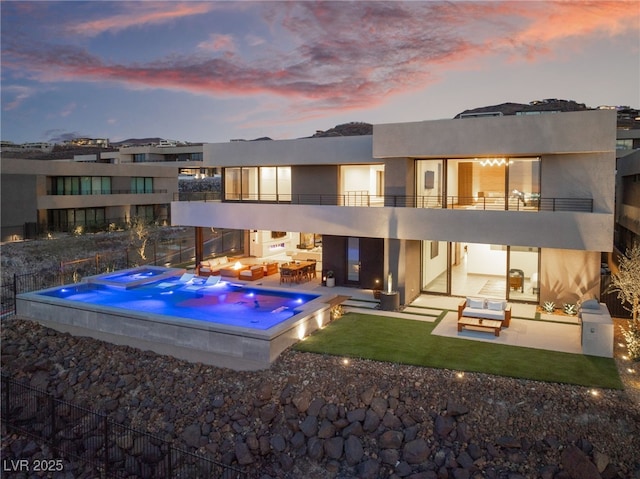 back of house at dusk with a patio, a balcony, a jacuzzi, and stucco siding