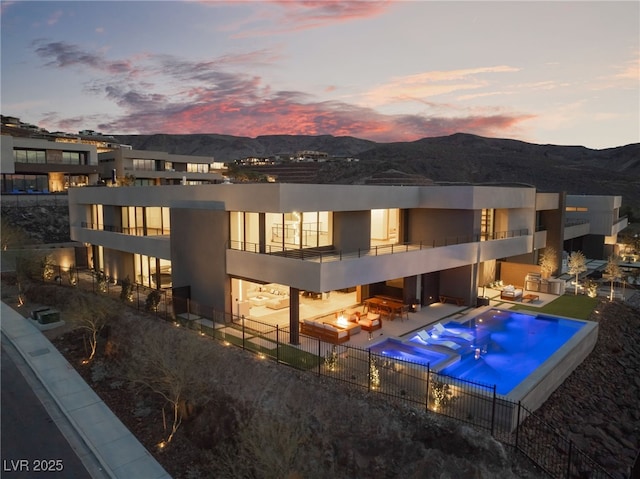 pool at dusk featuring a patio area, fence, a mountain view, and a community pool