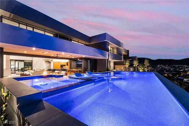 pool at dusk featuring an infinity pool and a patio