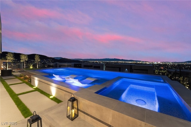 view of swimming pool featuring an infinity pool, an in ground hot tub, a patio, and a mountain view