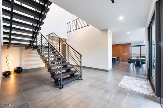 staircase featuring tile patterned flooring, wooden walls, baseboards, and recessed lighting