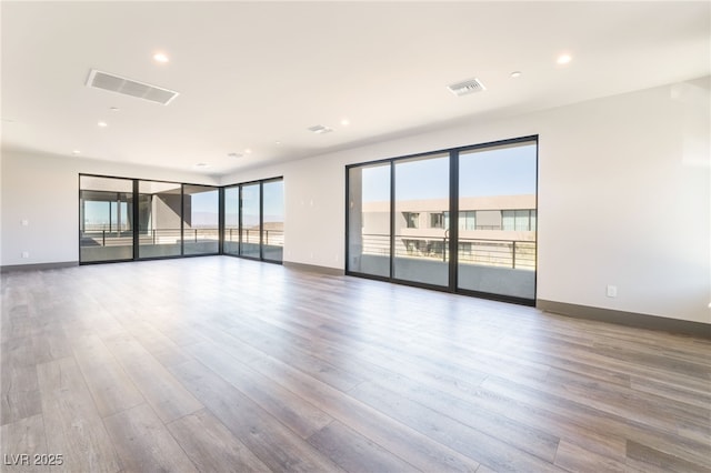 unfurnished room with baseboards, wood finished floors, visible vents, and a healthy amount of sunlight