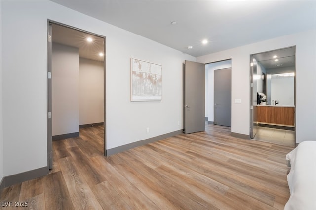 unfurnished bedroom with baseboards, ensuite bathroom, light wood-type flooring, a sink, and recessed lighting