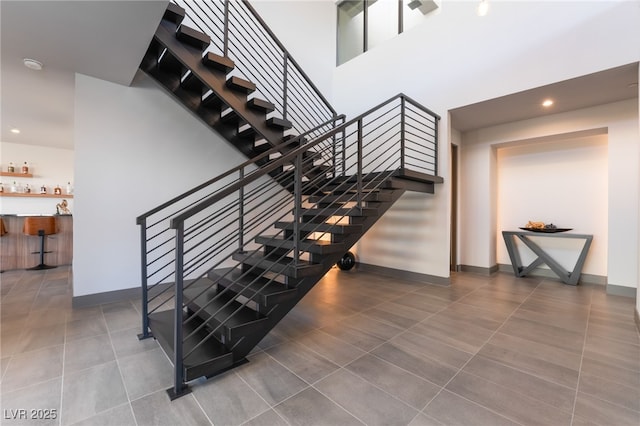 staircase featuring a dry bar, recessed lighting, a high ceiling, and baseboards