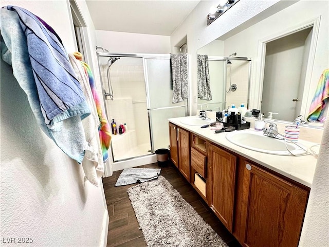 full bath with double vanity, a shower stall, a sink, and wood finished floors