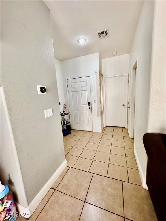 hallway with visible vents, baseboards, and light tile patterned floors