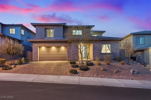 view of front of home with a garage, stone siding, decorative driveway, and stucco siding