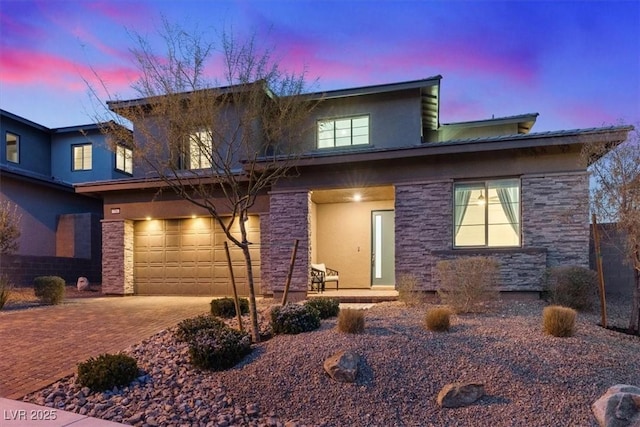 view of front of home with an attached garage, stone siding, decorative driveway, and stucco siding