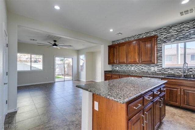 kitchen featuring visible vents, decorative backsplash, open floor plan, a kitchen island, and a sink