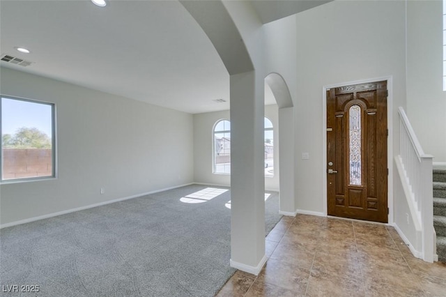 foyer entrance featuring arched walkways, light colored carpet, visible vents, stairway, and baseboards