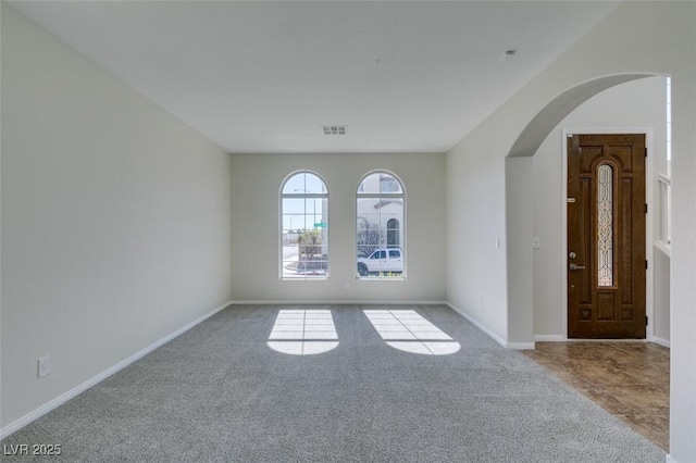 unfurnished room featuring arched walkways, light carpet, visible vents, and baseboards