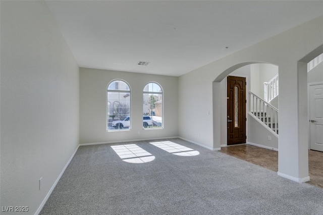 empty room featuring arched walkways, light colored carpet, visible vents, baseboards, and stairway