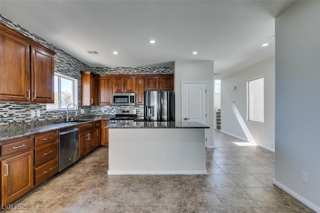 kitchen with a center island, backsplash, appliances with stainless steel finishes, a sink, and dark stone counters