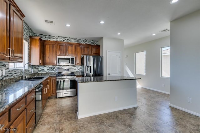 kitchen with dark stone counters, appliances with stainless steel finishes, a kitchen island, and visible vents