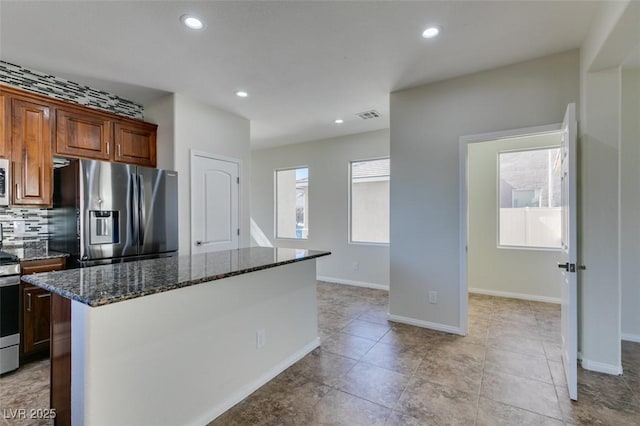 kitchen featuring a kitchen island, visible vents, appliances with stainless steel finishes, dark stone counters, and tasteful backsplash