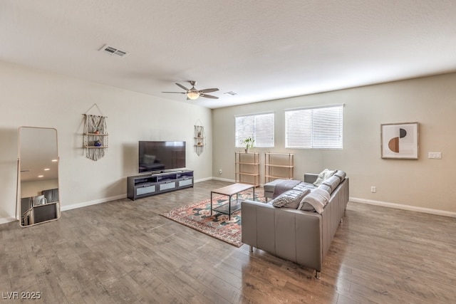 living room featuring a ceiling fan, wood finished floors, visible vents, and baseboards