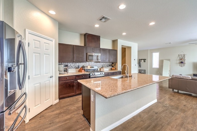 kitchen featuring a kitchen island with sink, a sink, visible vents, dark brown cabinets, and appliances with stainless steel finishes