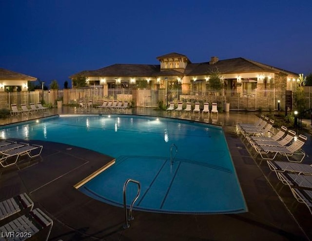 pool at twilight featuring a patio, fence, and a community pool