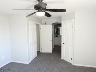 unfurnished bedroom with ceiling fan, dark carpet, and baseboards