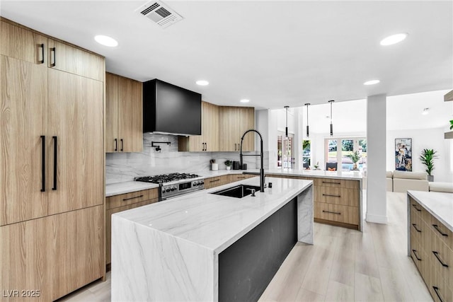 kitchen featuring visible vents, light stone countertops, a large island with sink, stainless steel stove, and a sink