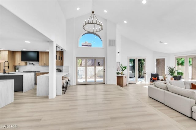 living area with visible vents, an inviting chandelier, french doors, light wood-style floors, and high vaulted ceiling