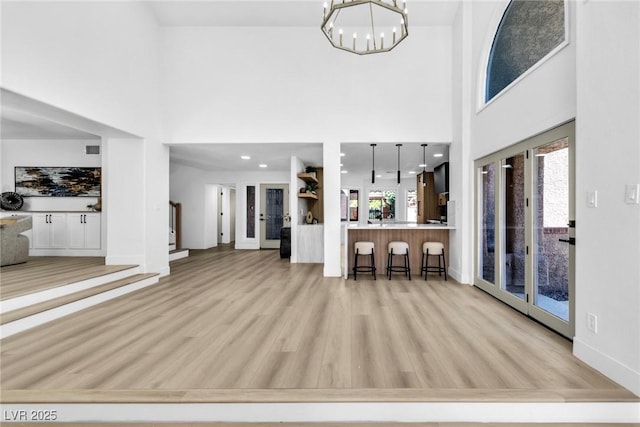 living room with a towering ceiling, light wood-style floors, plenty of natural light, and a chandelier