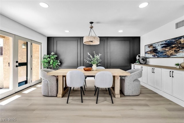 dining area with light wood finished floors, french doors, recessed lighting, and a decorative wall