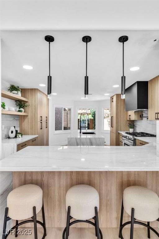 kitchen featuring wall chimney exhaust hood, modern cabinets, a breakfast bar area, decorative light fixtures, and open shelves