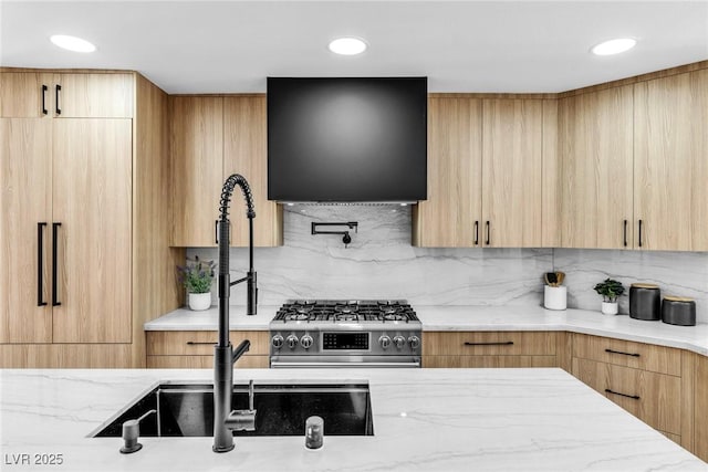 kitchen featuring stainless steel gas stove, modern cabinets, light stone counters, and a sink