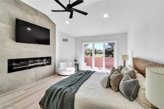 bedroom featuring visible vents, a tiled fireplace, wood finished floors, access to exterior, and vaulted ceiling