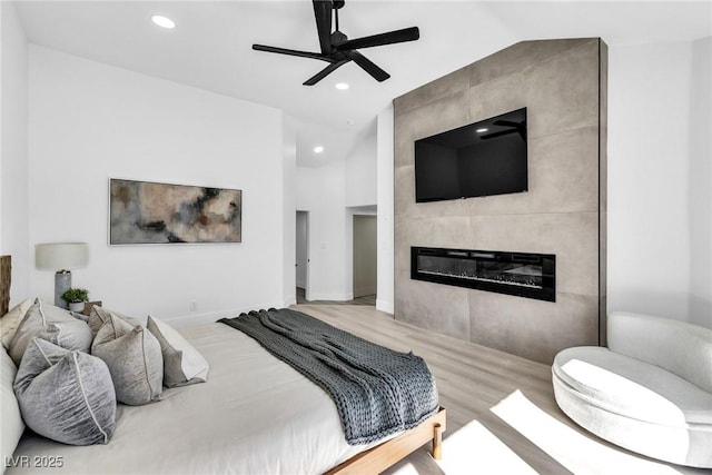 bedroom featuring light wood-style floors, vaulted ceiling, a tiled fireplace, and recessed lighting