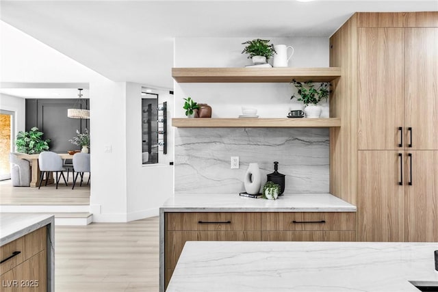 bar featuring pendant lighting, light wood-style flooring, baseboards, and backsplash