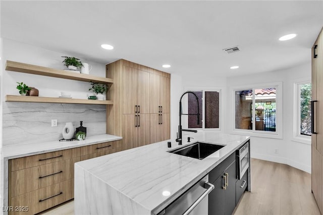 kitchen featuring stainless steel appliances, a sink, visible vents, open shelves, and an island with sink