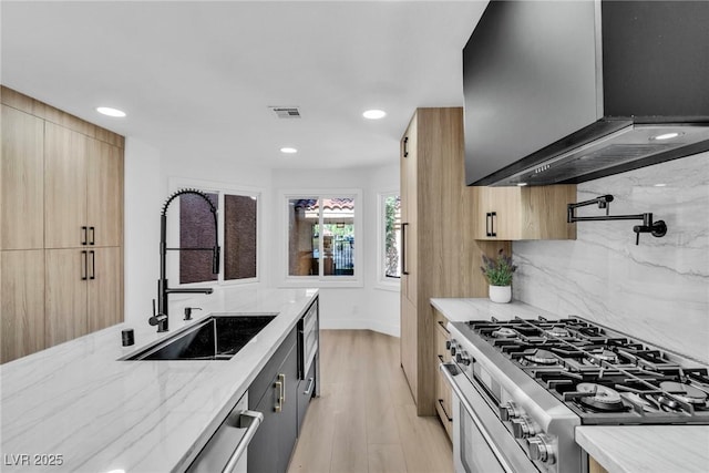 kitchen with light stone countertops, light wood-style flooring, decorative backsplash, a sink, and modern cabinets