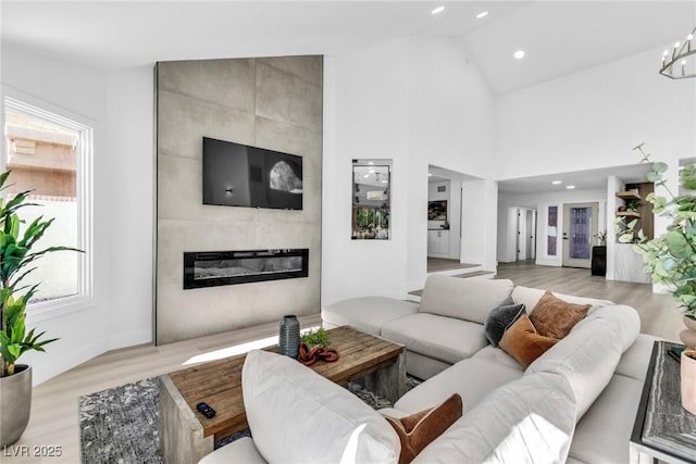 living room with high vaulted ceiling, a tile fireplace, recessed lighting, baseboards, and light wood-style floors